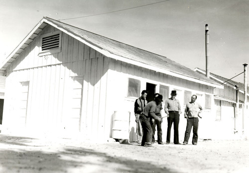 Five Mexican workers standing in front of labor camp buildings, Salinas, California