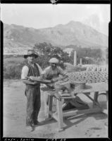 Two men making clay roofing tiles at a picnic table in Loja, Spain, 1929