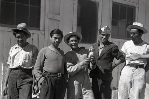 Five Mexican workers in front of camp building, one worker holding a baby doll