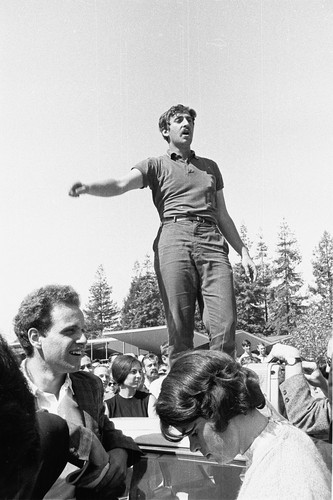 Jack Weinberg speaking from top of police car. Mario Savio standing on ground in foreground